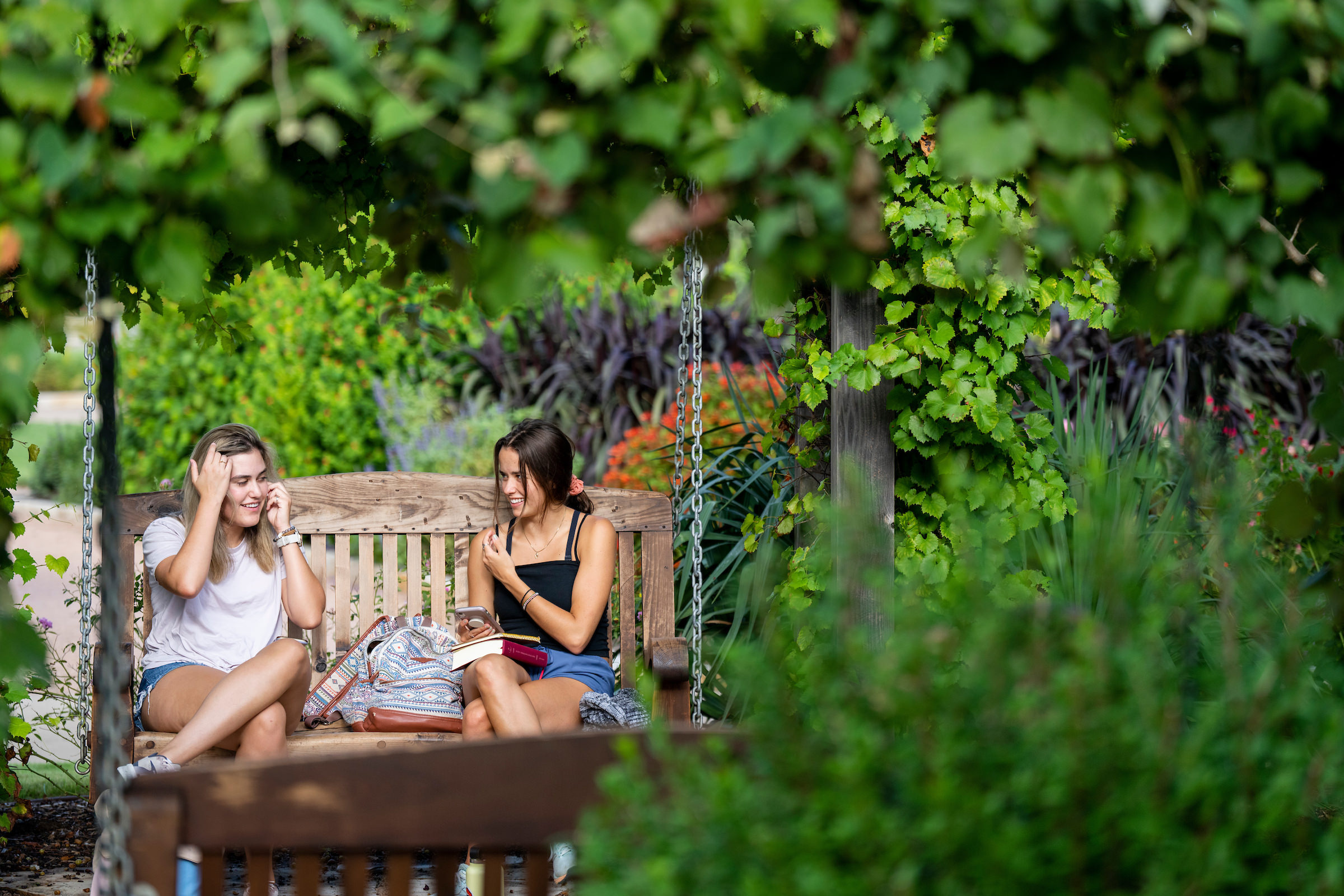 Two female students sitting on a bench talking in the Gardens.