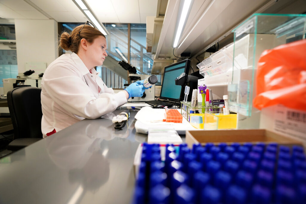 Woman wearing a protective lab coat and gloves analyzing data in a lab.