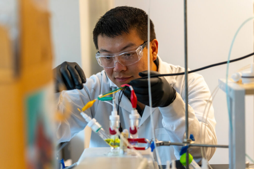 Student wearing protective lab gear and carefully measuing substances while conducting an experiment.